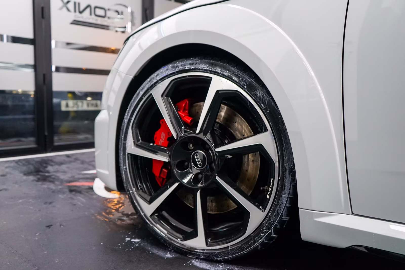 Black and polished alloy wheel with a red brake caliper on a white Audi