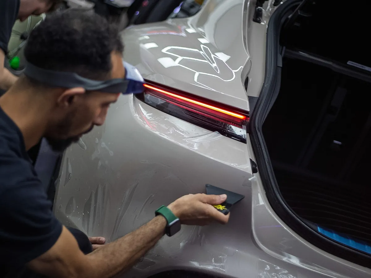 Iconix technician squeegeeing clear paint protection film onto a Porsche Taycan